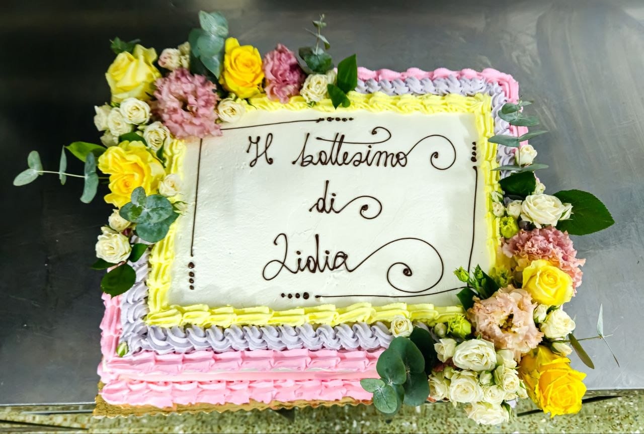 Torta da battesimo con bordi a crema colorata e corona di fiori freschi ed eucalipto
