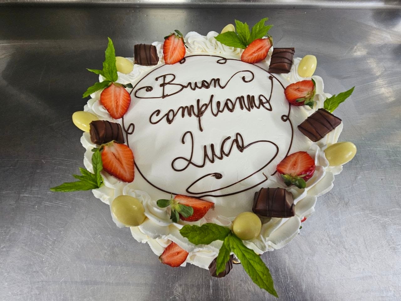 Torta di compleanno alla panna con fragole, menta e cioccolatini, scritta a mano libera