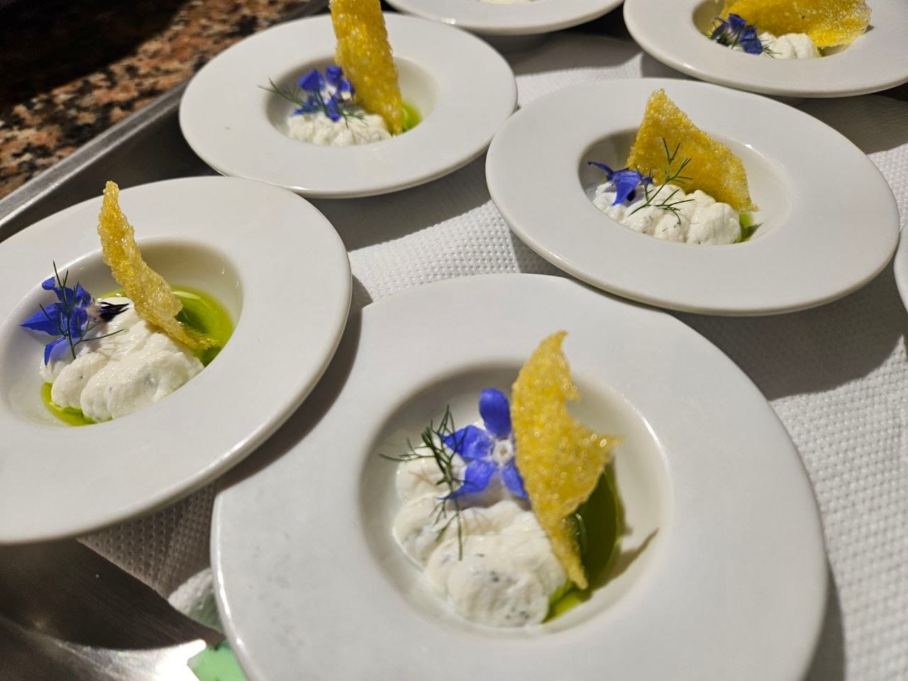 Piatti fondi con crema di formaggio, olio al basilico, cialda di grana e fiore di borragine