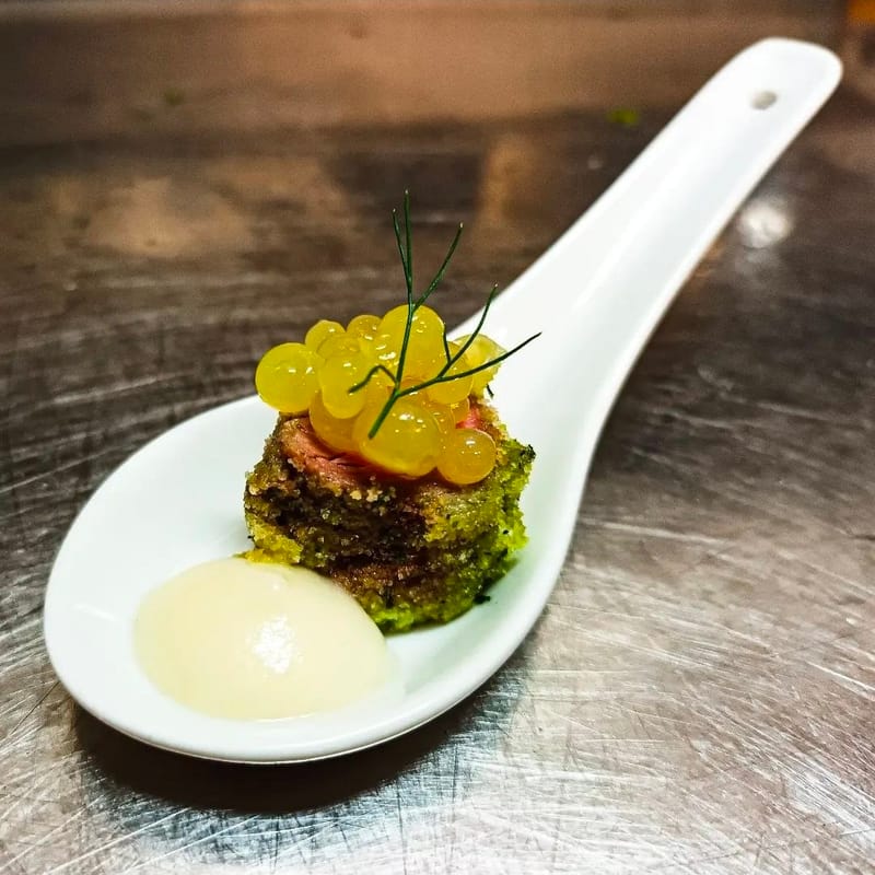 Cucchiaio gourmet con tonno in crosta di erbe, sfere di agrume e crema, guarnito con aneto