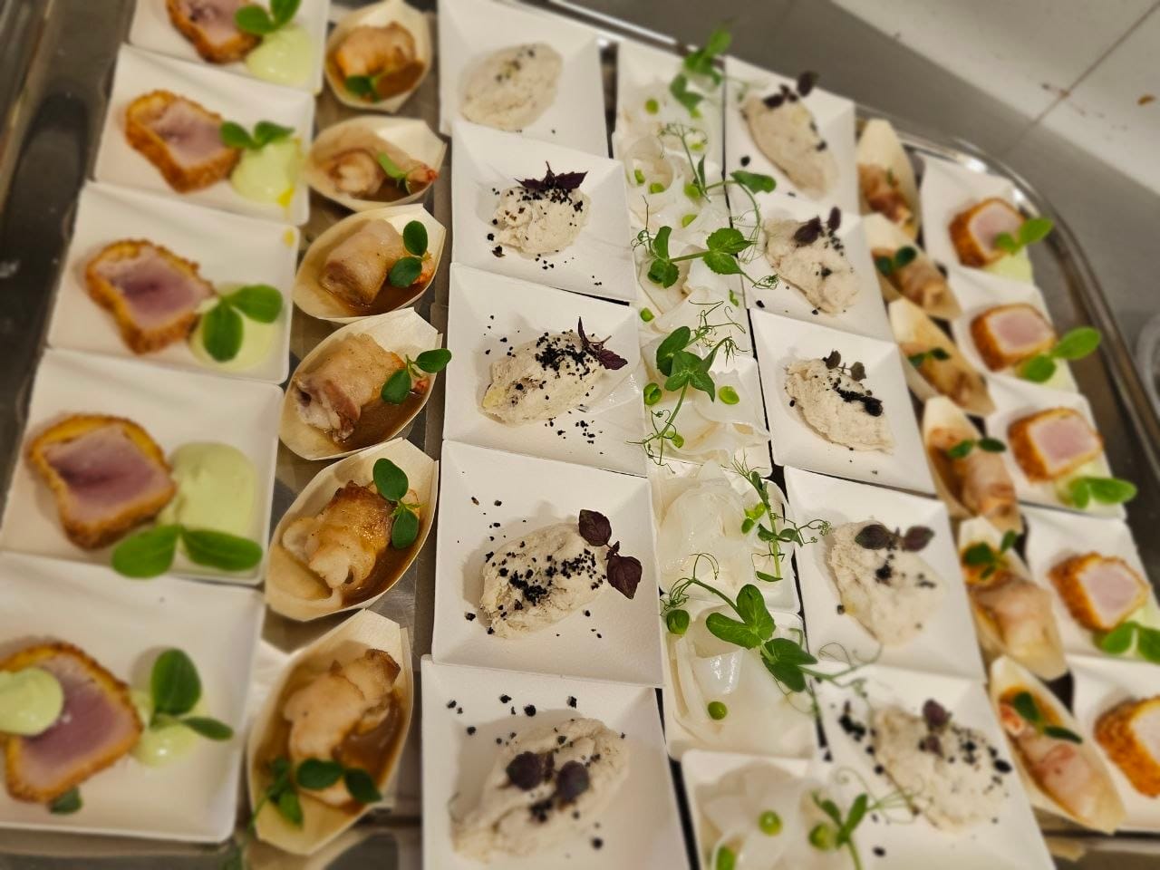 Mise en place di finger food gourmet impiattati uno per uno su piattini bianchi