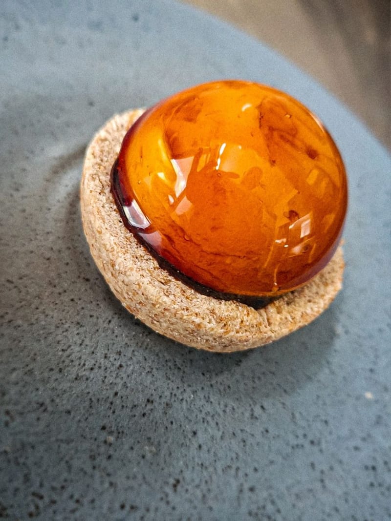 Finger food gourmet: sfera lucida agli agrumi su base di pane croccante, servita su ceramica grigia