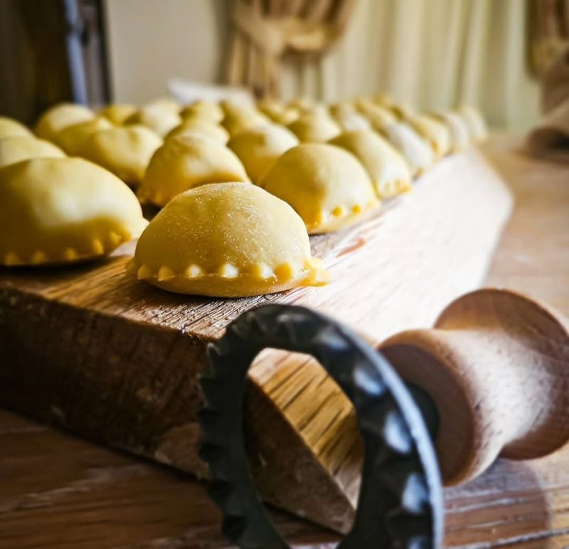 Panadine appena chiuse su tagliere di legno, accanto alla rotella tagliapasta